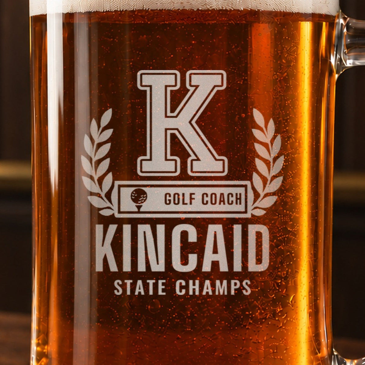 Close-up of a golf coach beer stein engraving, varsity K in a laurel wreath, GOLF COACH bar, KINCAID and STATE CHAMPS, through amber beer