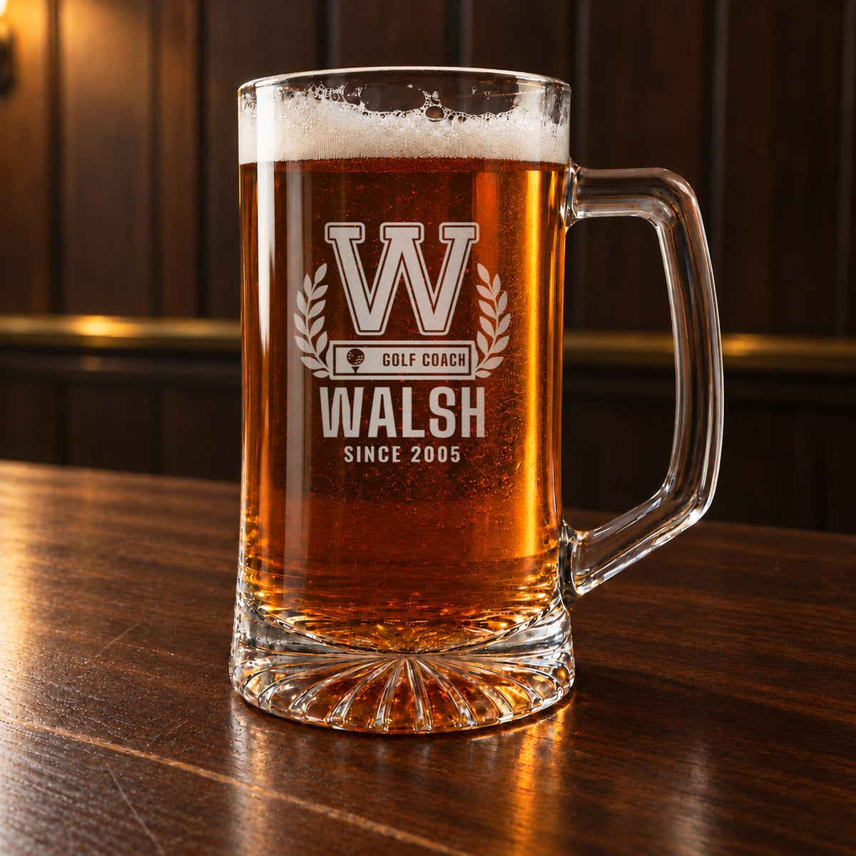 Personalized golf coach beer stein engraved with a varsity W, laurel wreath, GOLF COACH bar, WALSH and SINCE 2005, filled with beer on a dark bar