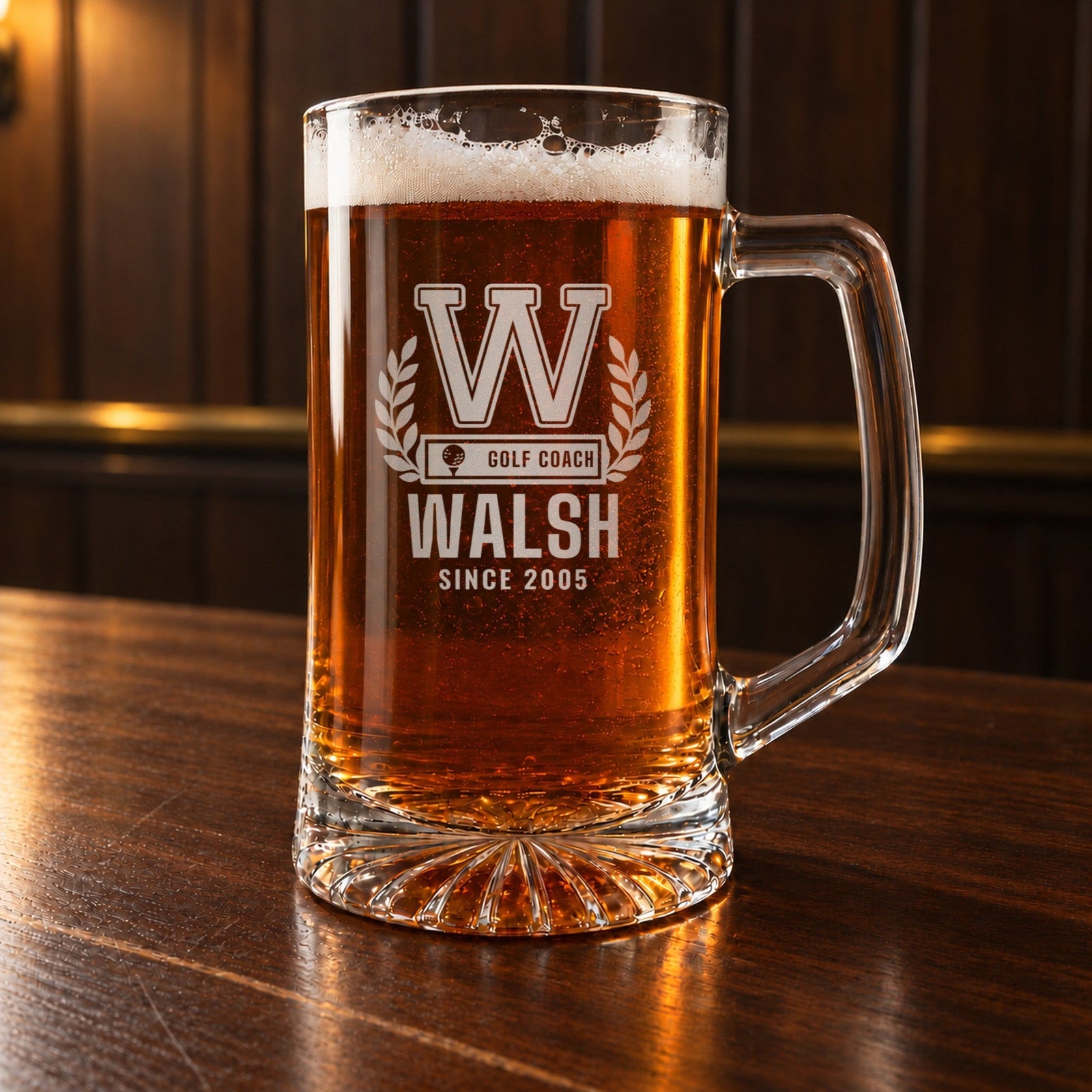 Personalized golf coach beer stein engraved with a varsity W, laurel wreath, GOLF COACH bar, WALSH and SINCE 2005, filled with beer on a dark bar