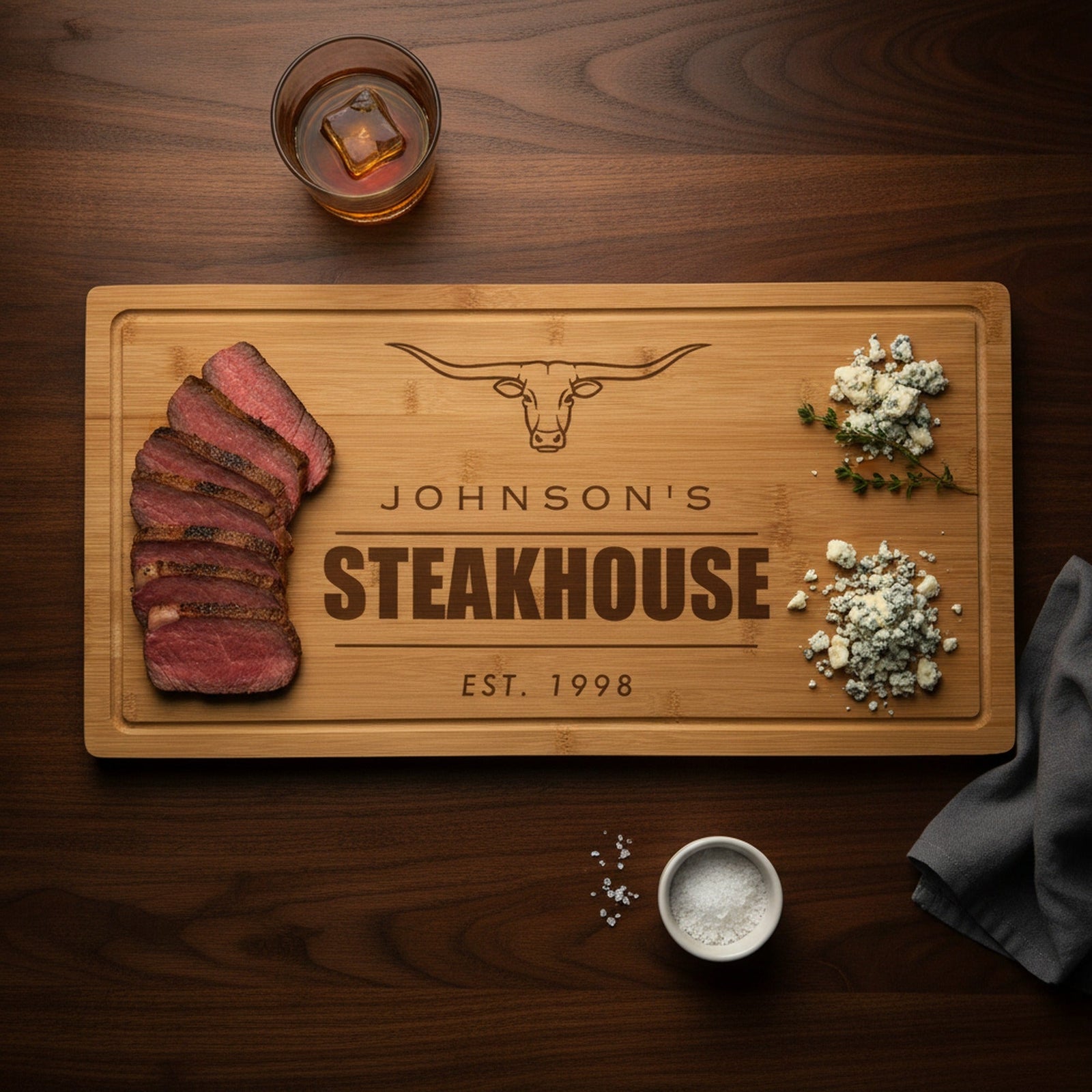 Personalized steakhouse cutting board engraved Johnson's Steakhouse Est. 1998 on a walnut bar top with sliced ribeye, a gift for a golfer who loves steak