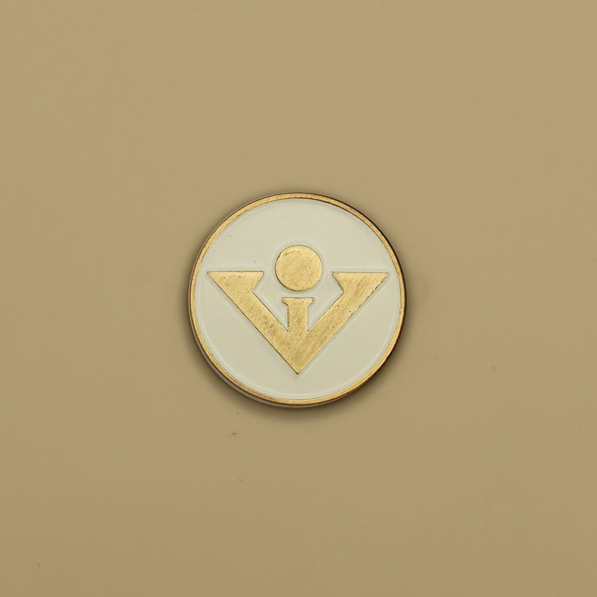 Round cream and gold golf ball marker with stylized figure design in raised gold relief on center circle with gold-tone rim