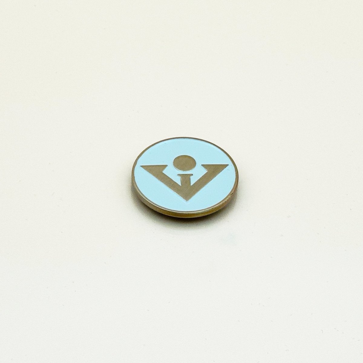 Light blue circular ball marker with brass rim and bronze golfer figure icon in center, displayed on neutral background