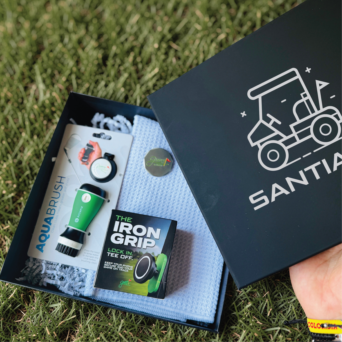 Personalized golf gift box with a name-engraved navy lid, open to show the AquaBrush club cleaner, waffle towel, ball marker and Iron Grip phone mount.